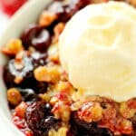 A close up of a bowl of cherry crisp with a scoop of vanilla ice cream