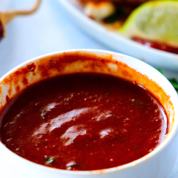 A bowl of Guajillo Sauce in the foreground with a plate of quesadillas in the background