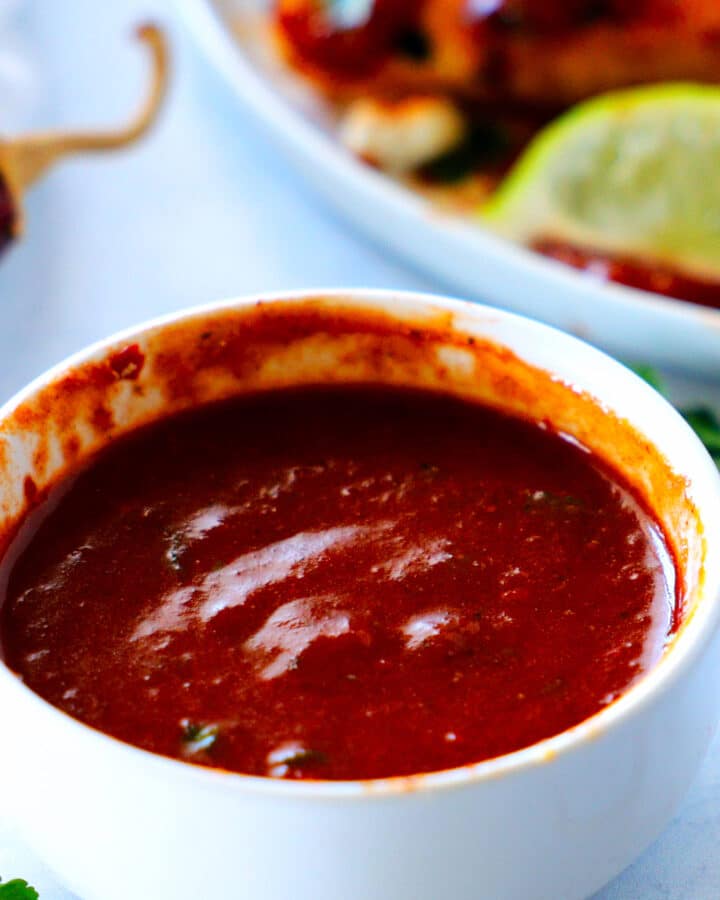 A bowl of Guajillo Sauce in the foreground with a plate of quesadillas in the background