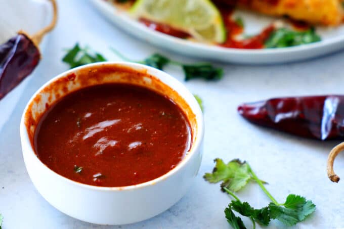 a bowl of guajillo sauce with peppers and cilantro sitting beside it