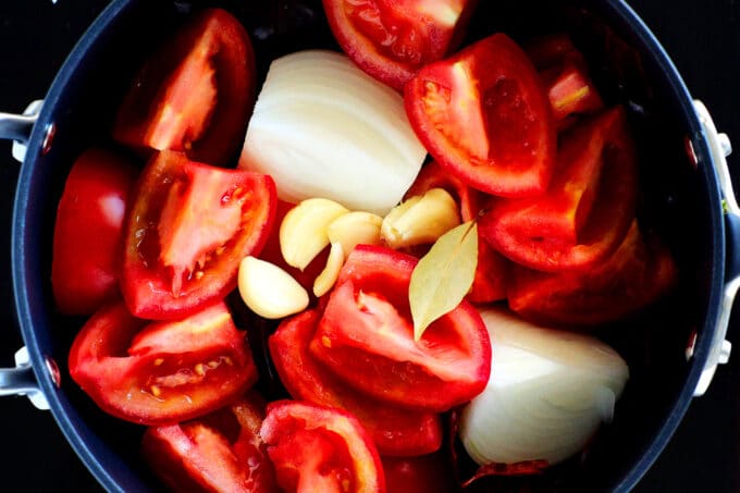 an overhead view of uncooked tomatoes, garlic, and onions in a pan