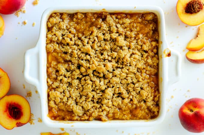 overhead view of peach crisp with sliced peaches beside it