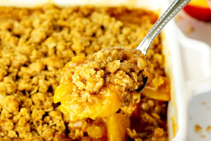 a close up of a spoonful of peach crisp with the pan of it in the background