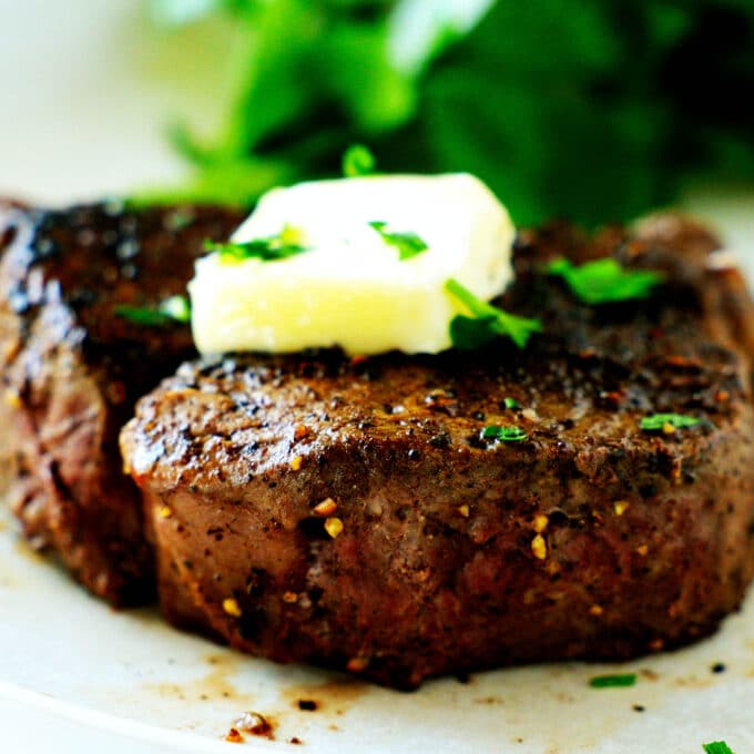 A close up of the side of a filet mignon with a pat of butter and herbs on top