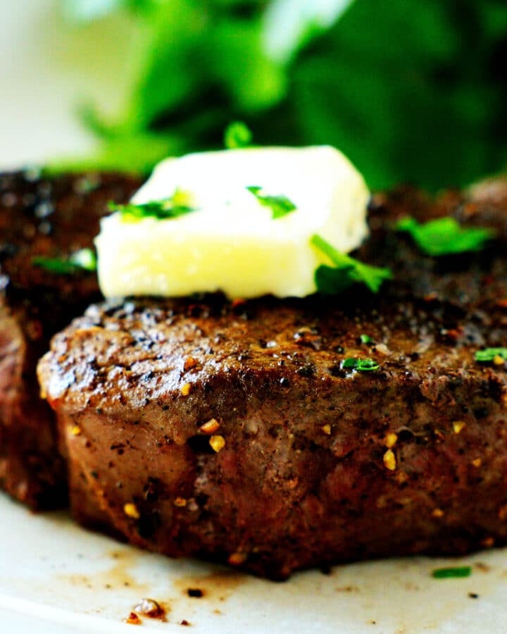 A close up of the side of a filet mignon with a pat of butter and herbs on top