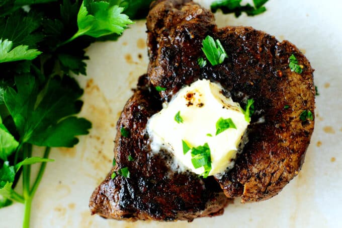 an overhead view of a filet mignon with a pat of butter and herbs on top
