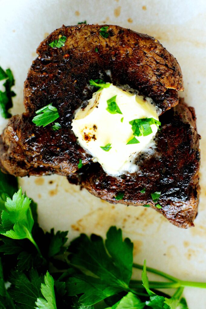 an overhead view of a filet mignon with a pat of butter and herbs on top