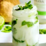A coconut mojito in a jar with a coconut and limes in the background