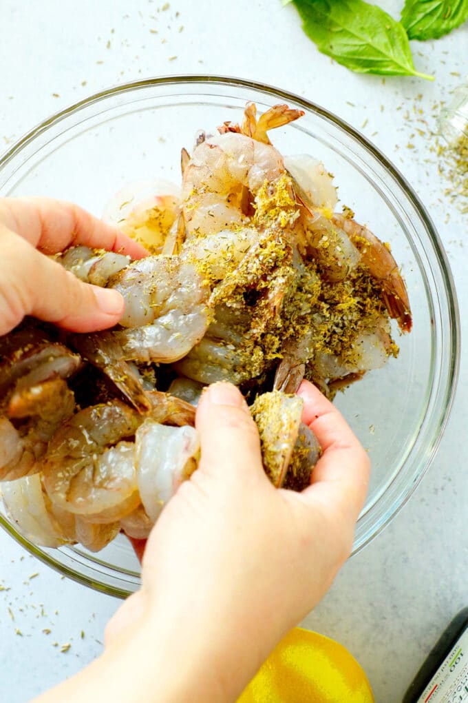 Hands mixing seasoning into raw shrimp