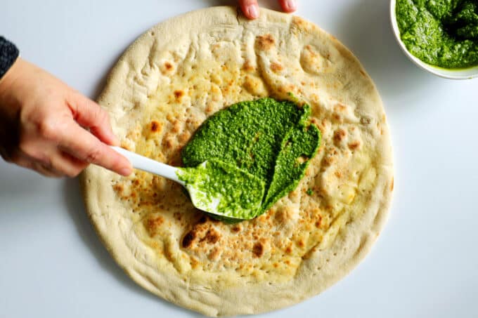 homemade pesto being spread over a pizza crust