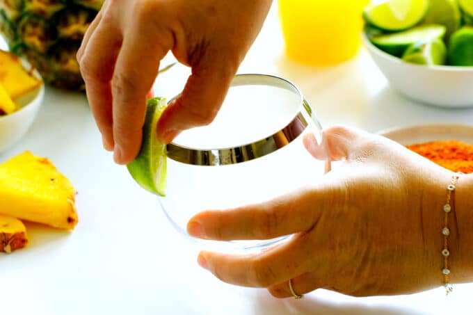 hands applying lime juice to the side of a glass with a lime wedge