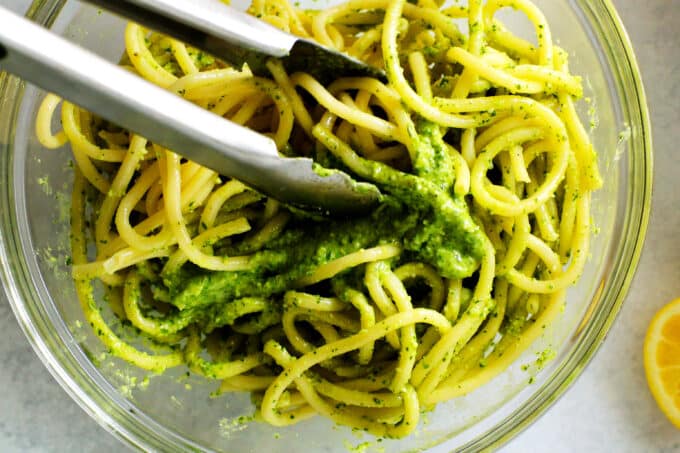 tongs being used to incorporate pesto sauce into pasta