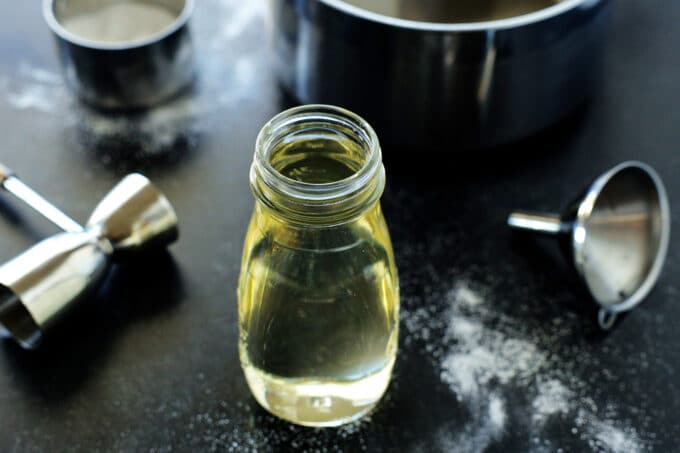 A bottle of simple syrup sitting on a counter with a funnel, sauce pan, and measuring cup