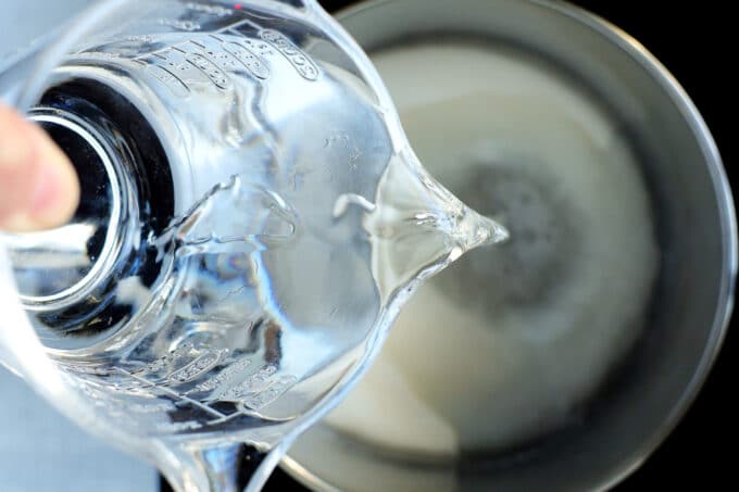 Water being poured from a measuring pitcher into a sauce pan with sugar in it