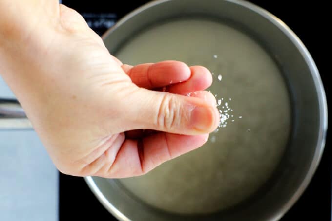a hand sprinkling salt into a sauce pan of simple syrup