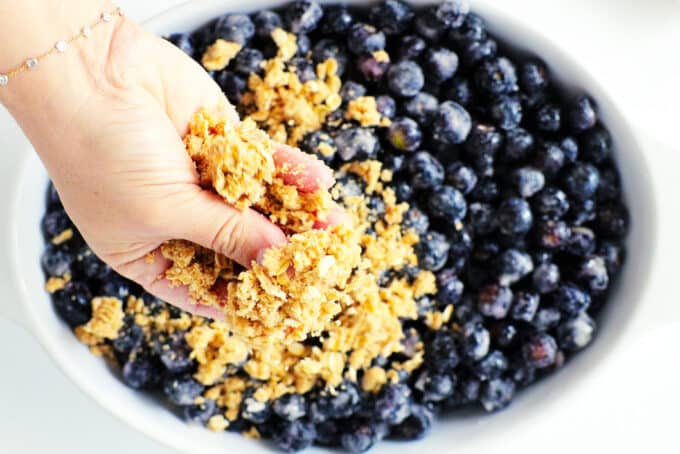 a hand crumbling crisp topping over blueberries