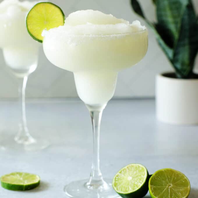 A frozen margarita in a margarita glass with a lime wheel on the side