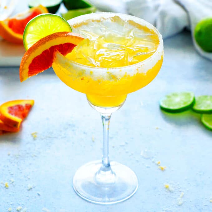 an Italian Margarita with lime wheel and orange wedge on the side and citrus slices in the background
