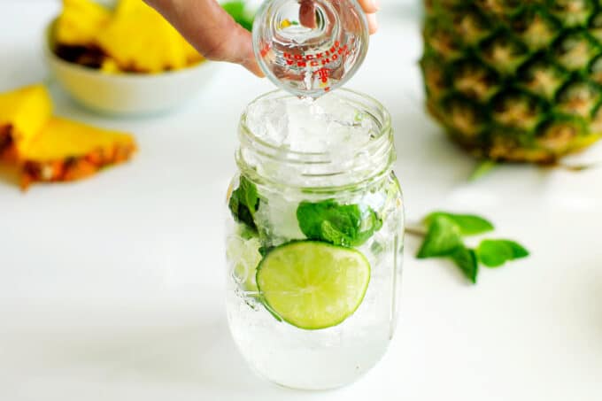 Rum being poured into a mason jar with ice, mint, and lime
