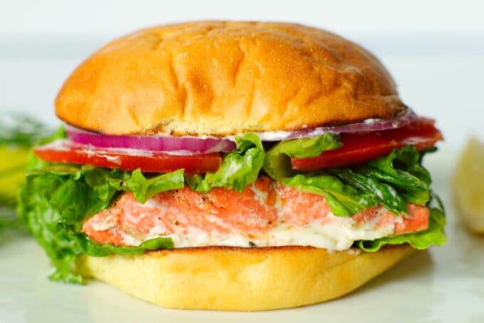 A side view of a fully assembled salmon sandwich with red onions, tomatoes, and lettuce