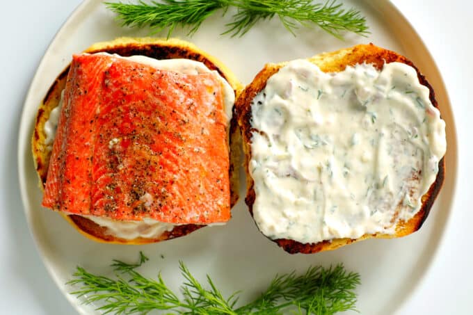 A toasted bun with dill sauce and a salmon filet on top