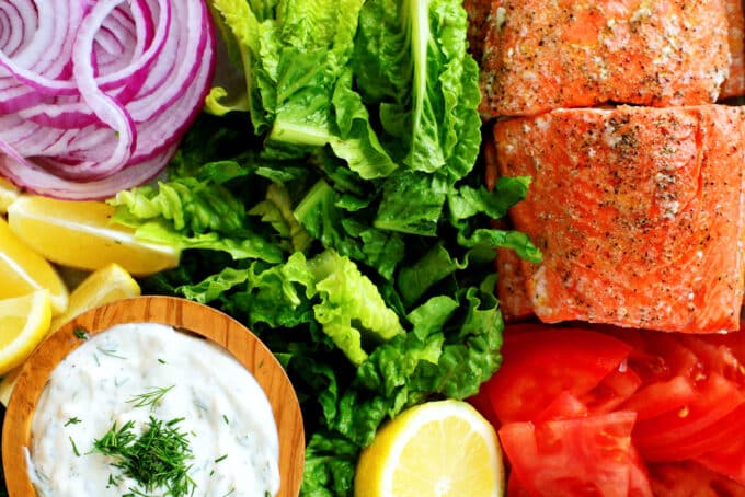 an overhead view of Salmon, dill sauce, red onion, lemon, tomatoes, and lettuce.