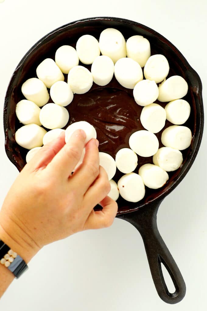 a hand placing marshmallows on top of melted chocolate in a pan