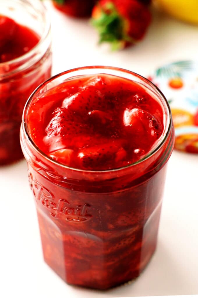 A jar of strawberry compote and fresh strawberries in the background