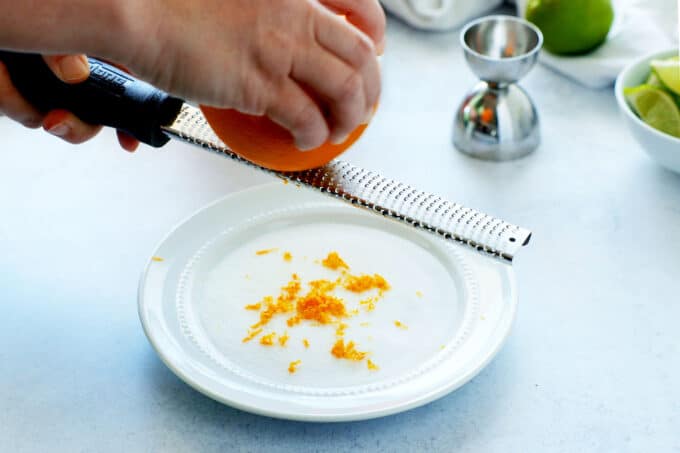 Hands zesting an orange onto a plate