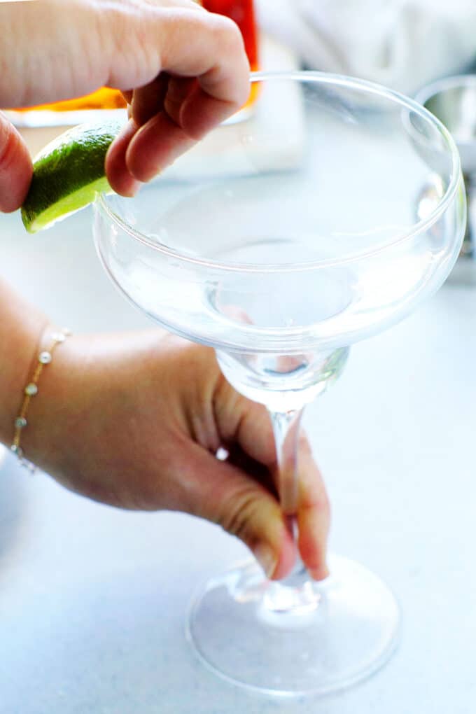 hands running a lime wedge along the rim of a margarita glass