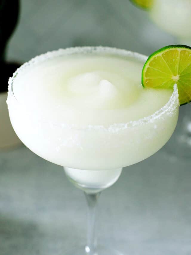A frozen margarita in a margarita glass with a lime wheel on the side