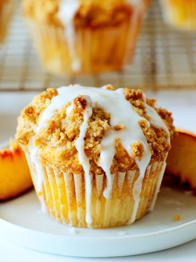 a beautiful peach muffin on a plate with muffins and peaches in the background