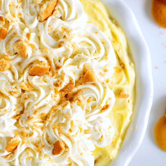 an overhead view of A banana pudding cheesecake in a pie plate, the whipped cream piped in swirls on top with a sprinkling of crushed vanilla wafers