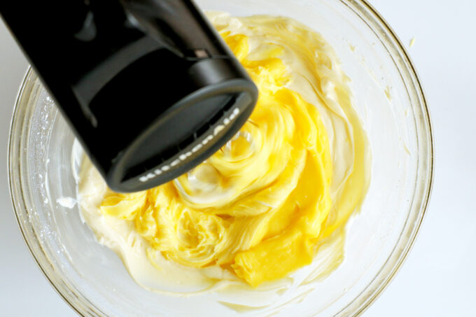 a hand mixer being used to mix the cream cheese and pudding mixtures