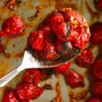 a metal serving spoon full of blistered tomatoes with basil