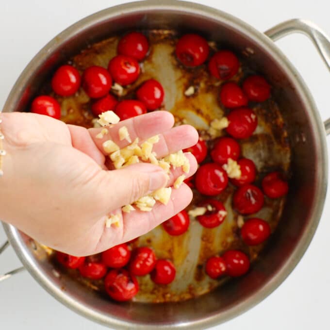A closeup of someone sprinkling minced garlic into the pan of tomatoes