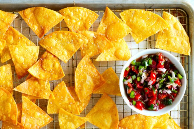 An overhead view of tortilla chips cooling on a rack with a bowl of pico de Gallo 