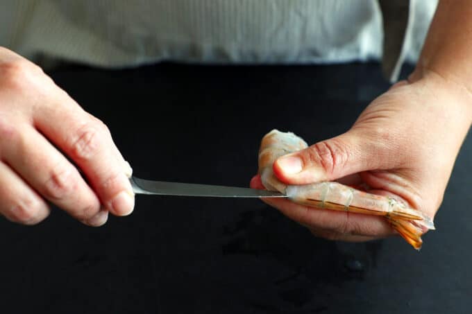 Someone using a pairing knife to slice down the back of a shrimp