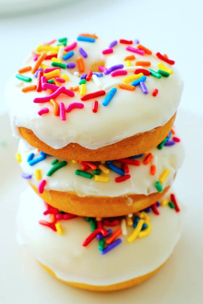 A stack of three donuts with vanilla glaze and colorful sprinkles