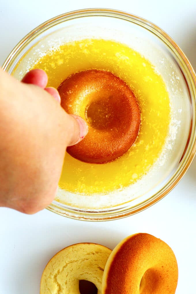 a hand dipping a baked donut into melted butter
