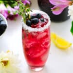 A blueberry cocktail with a sugar rim and blueberries and thyme for garish