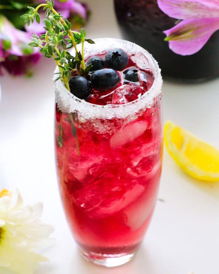 A blueberry cocktail with a sugar rim and blueberries and thyme for garish