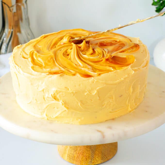 a knife is used to swirl caramel sauce around the top of an iced cake