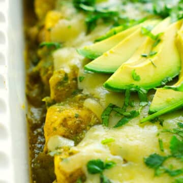A look down the row of rolled up enchiladas in a pan with green sauce and avocado