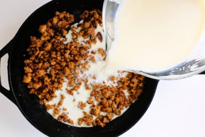 whole milk being poured into a skillet of sausage