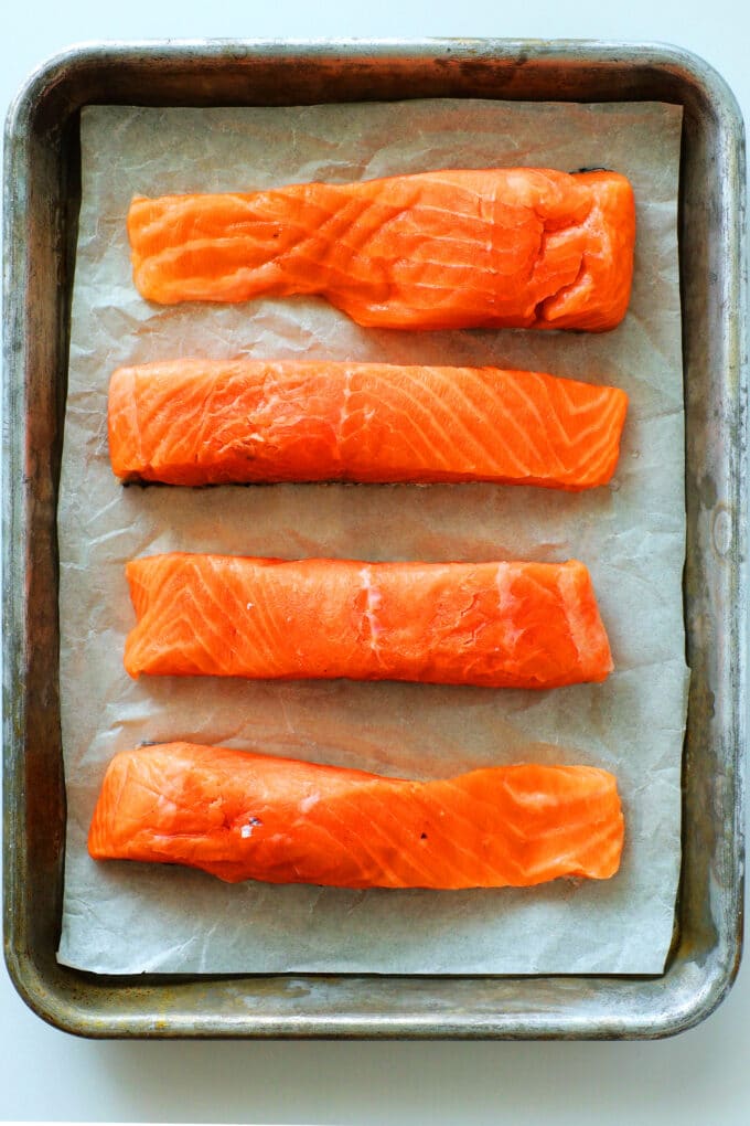 uncooked salmon fillets lined up on a baking sheet
