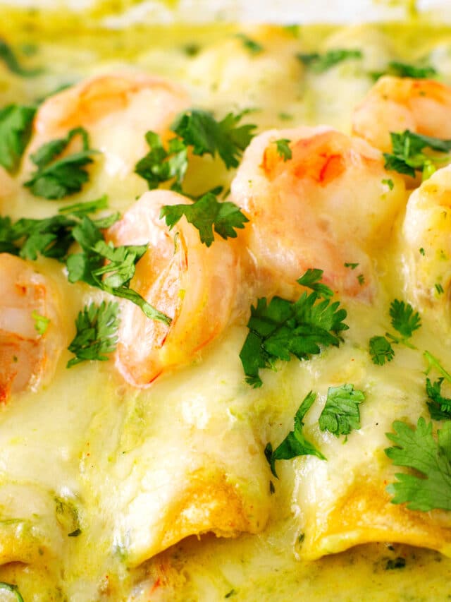 Shrimp enchiladas, still in the baking dish, with melty cheese, green sauce, and shrimp on top, with a cilantro garnish
