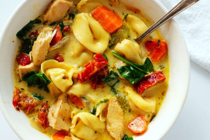 An overhead view of bright and vibrant Chicken Tortellini Soup in a white bowl with a spoon