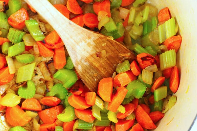 carrots, onion, and celery being sautéed in a pan with a wooden spoon