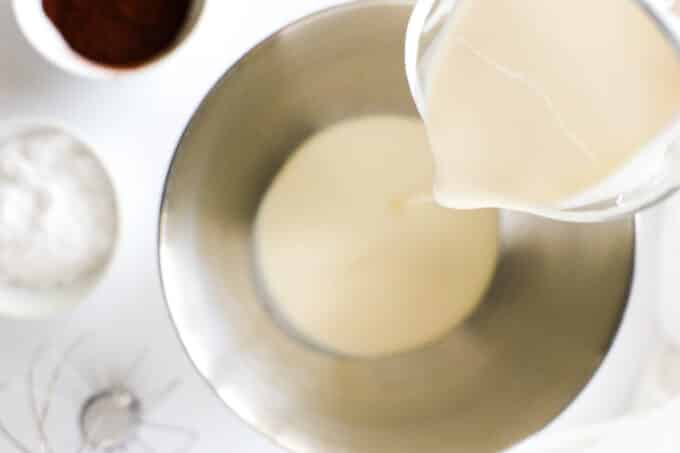 An overhead shot of heavy cream being poured from a measuring pitcher into a metal bowl